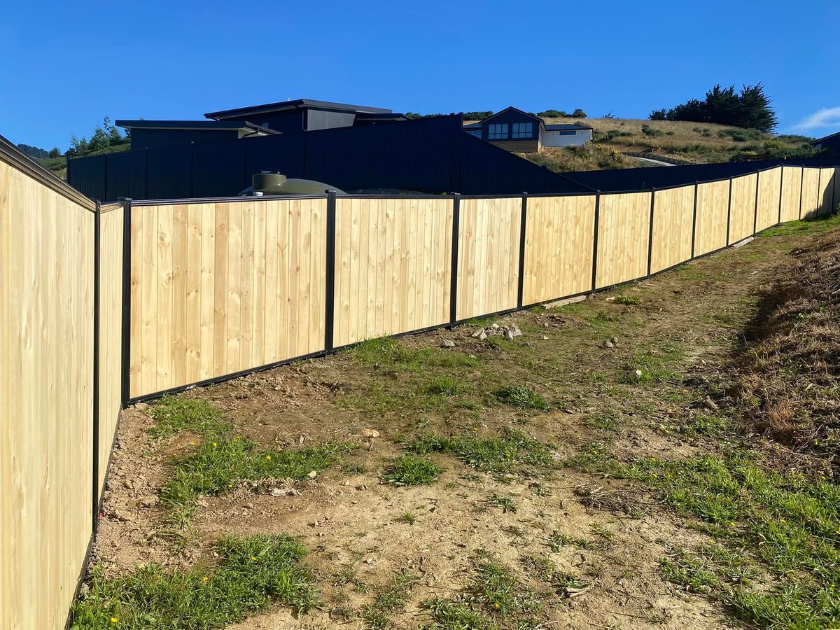 Timber paling fence stepping down a bank with colour steel fencing running behind it