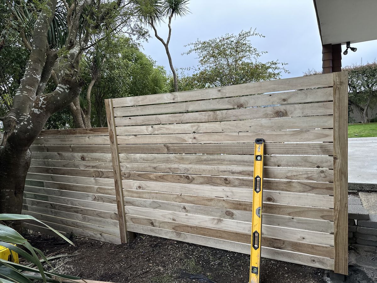 Horizontal timber fence part way through construction with a level held against the boards