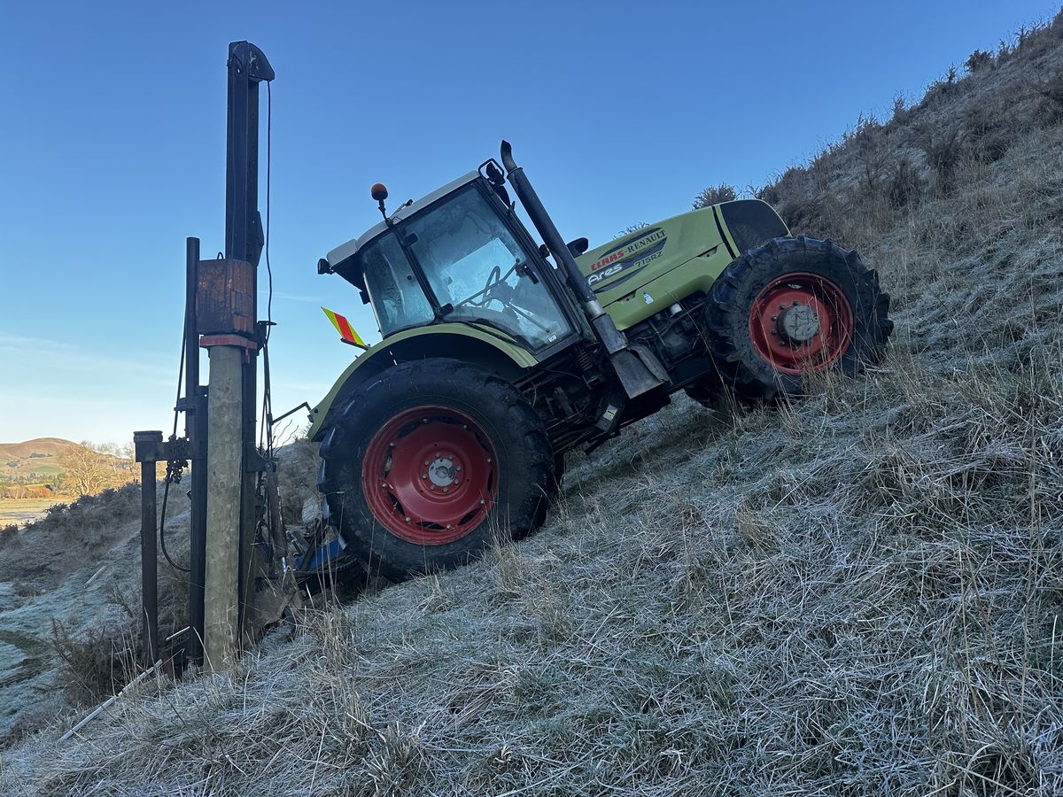 Tractor-mounted post driver working a new fence line on a steep frosty hillside