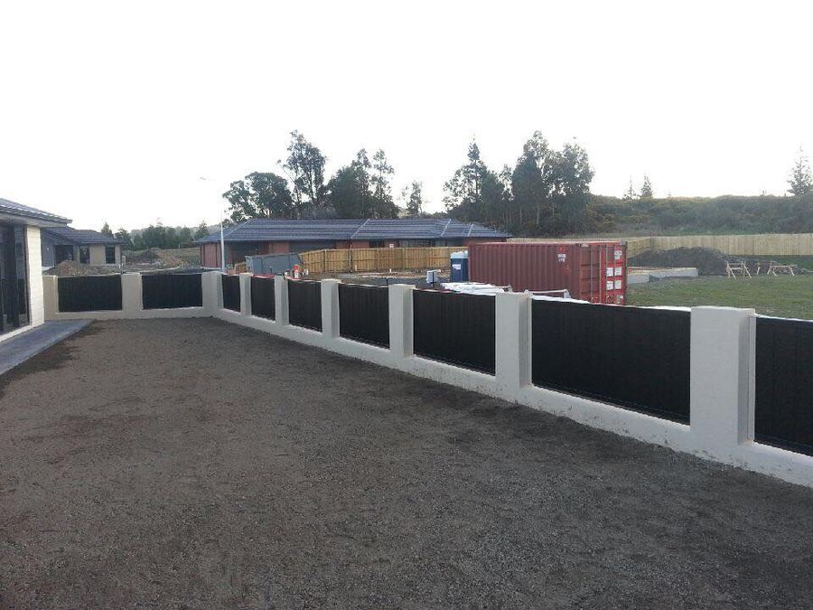 Dark colour steel infill panels between white concrete pillars on a new subdivision boundary
