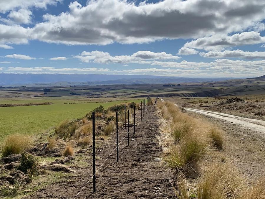 Post and waratah fence line running across high country above a gravel road