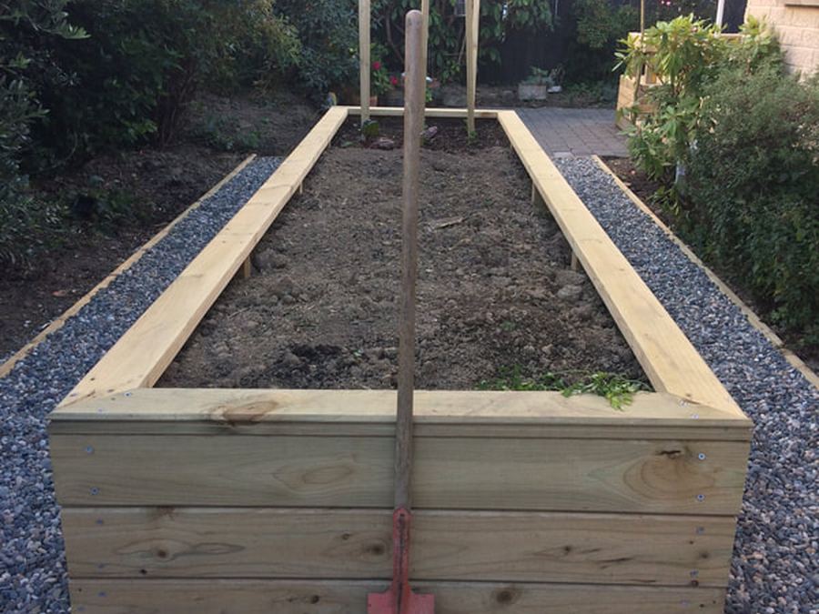 Timber raised garden bed built beside a gravel path, with a spade standing in the soil