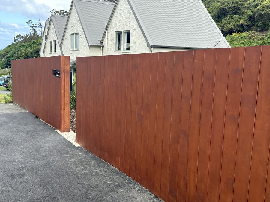Tall dark stained timber paling fence running along a townhouse driveway