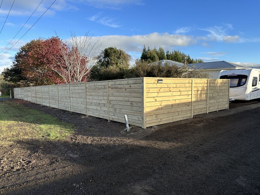 Horizontal timber fence enclosing a gravelled area with a caravan parked behind it