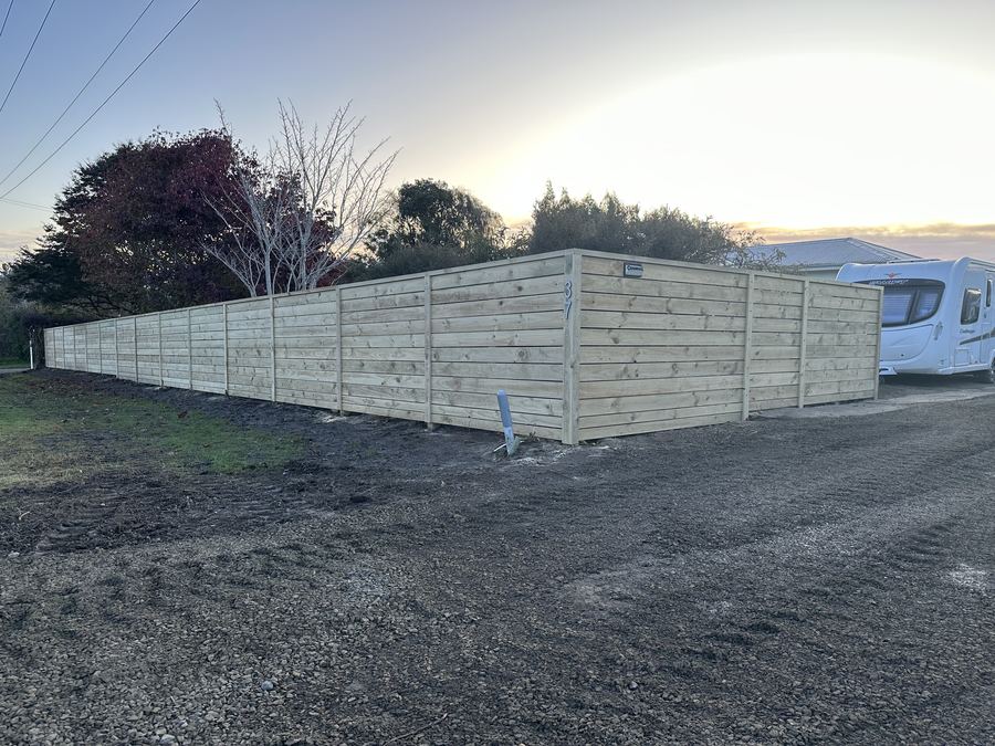 Horizontal timber fence enclosing a gravelled parking area, photographed at sunset