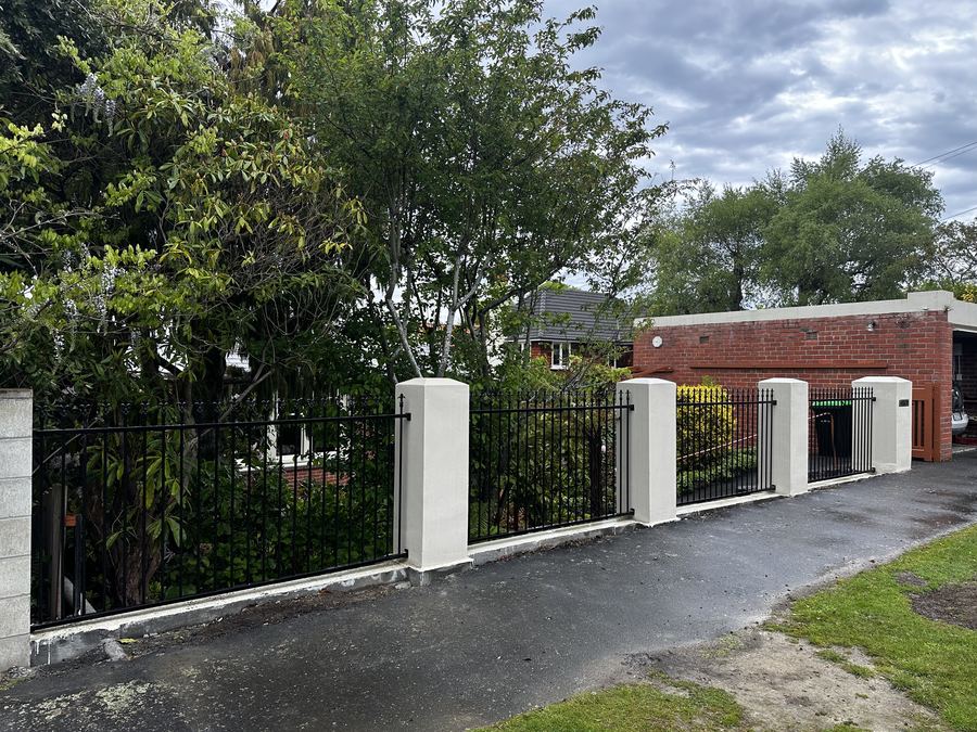 Black steel fence panels set between white plastered pillars on a brick wall