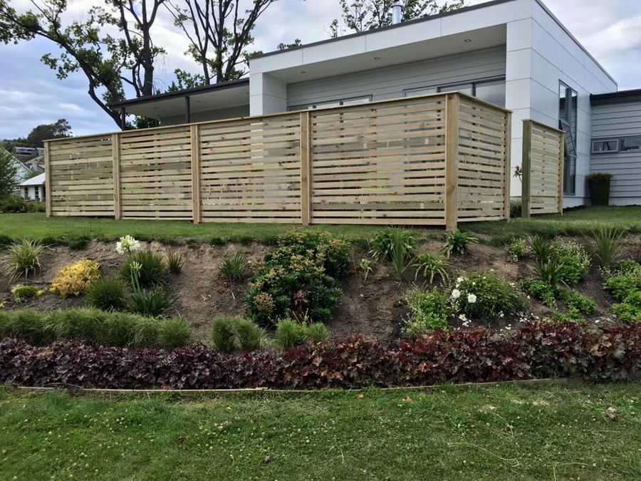 Horizontal slat screening panels above a landscaped bank at a modern house