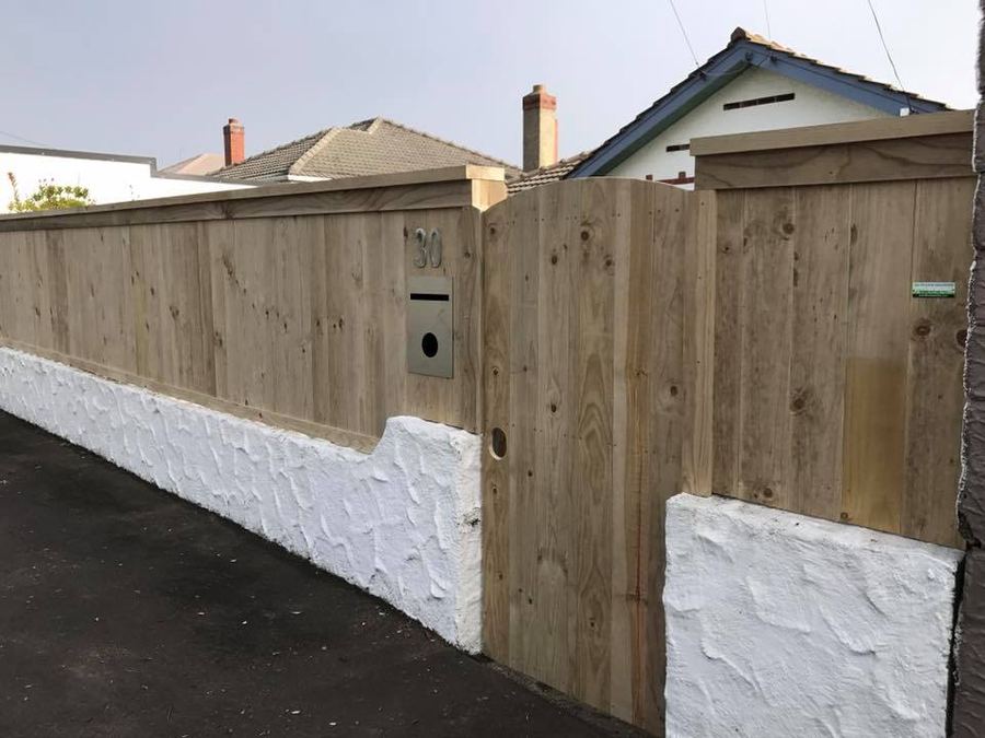 Timber fence built on top of a white plastered wall along a footpath