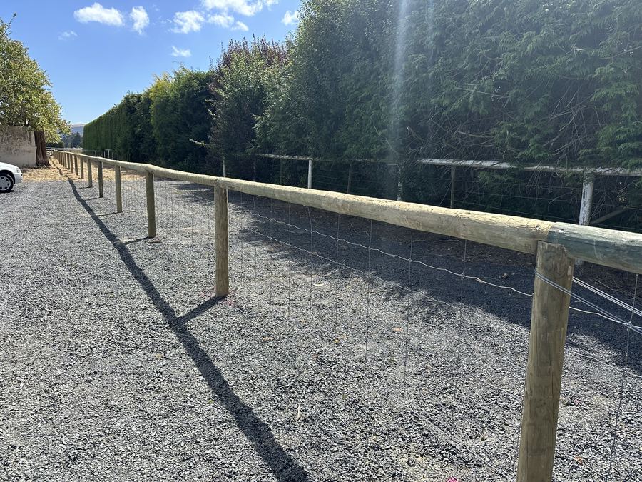 Post and wire netting fence enclosing a gravelled yard beside a shelter hedge
