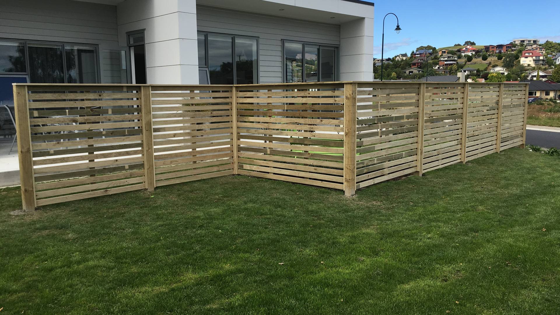 Horizontal timber slat fence enclosing the lawn of a modern grey house