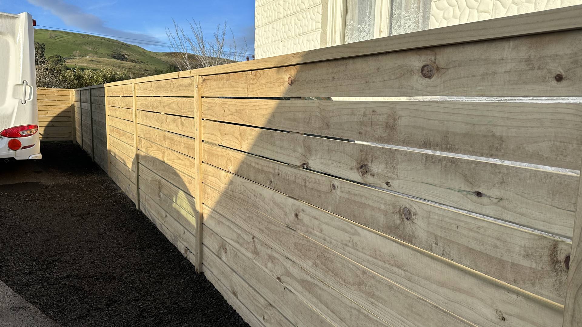 Horizontal timber board fence running the length of a driveway with hills behind