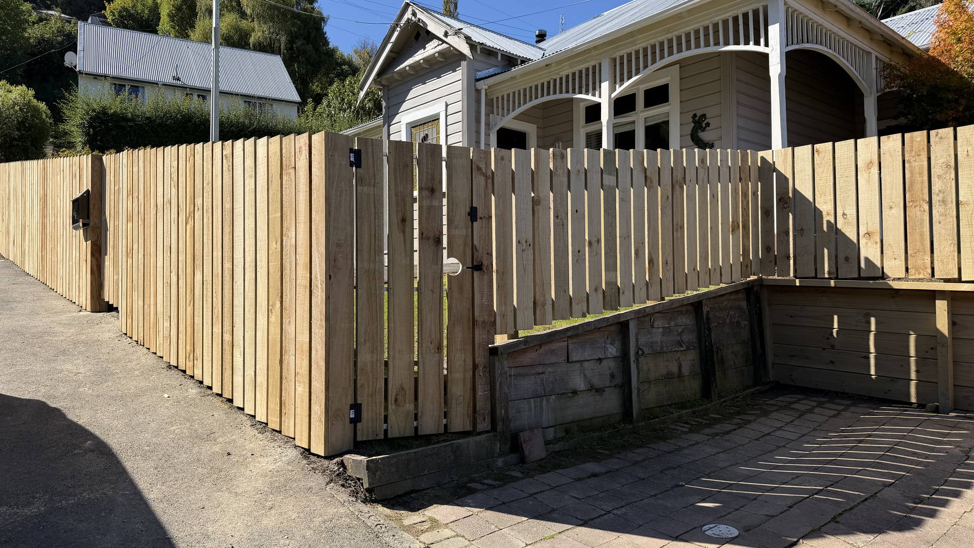 Timber picket fence and gate outside a weatherboard villa, with solid paling alongside