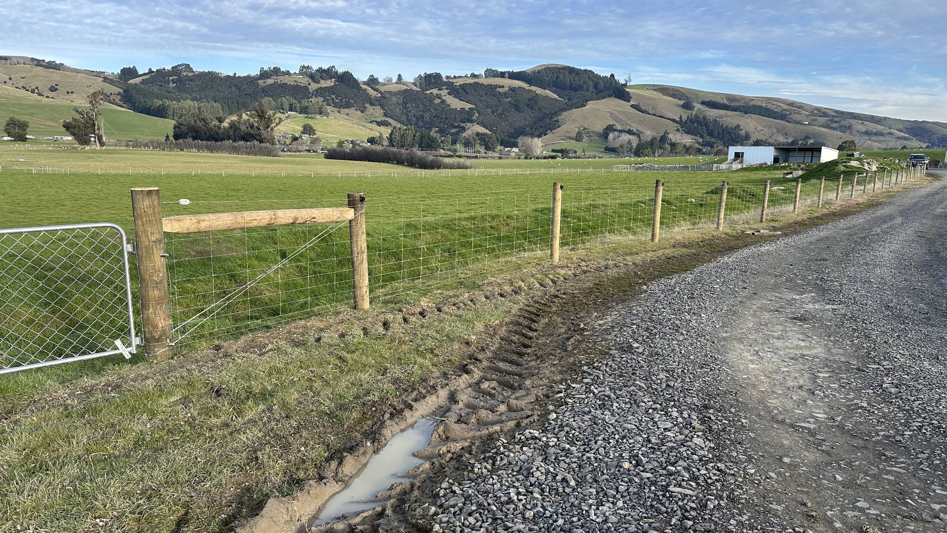 Netting farm fence running beside a gravel race with rolling Otago hills behind