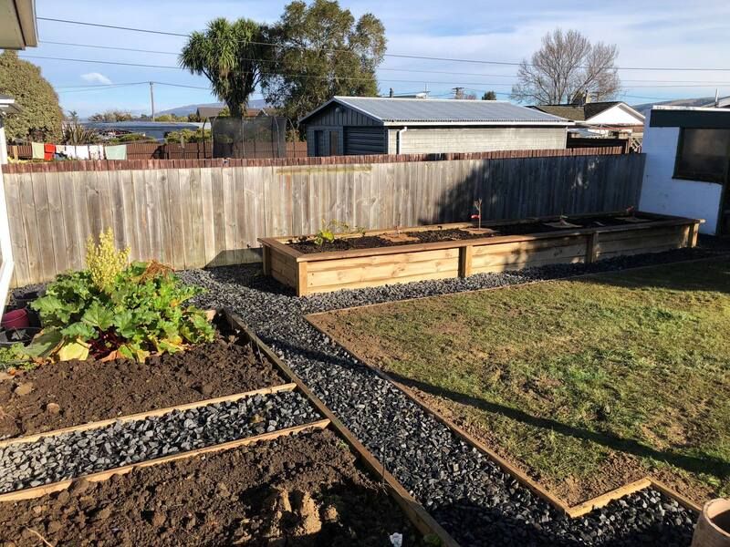 Two timber raised garden beds planted out in a back garden with gravel paths
