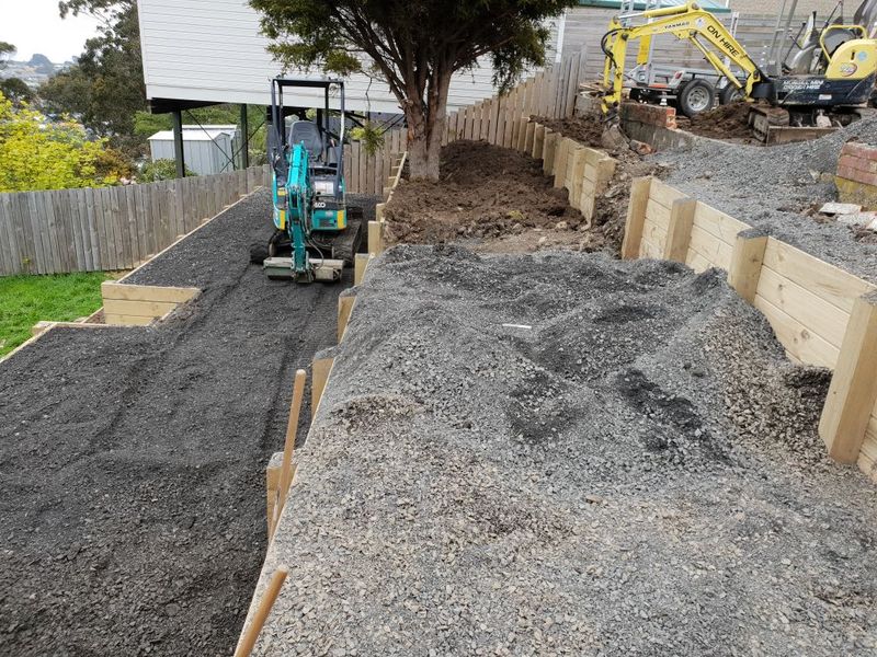 Timber retaining wall going in along a sloping boundary with a digger working behind it