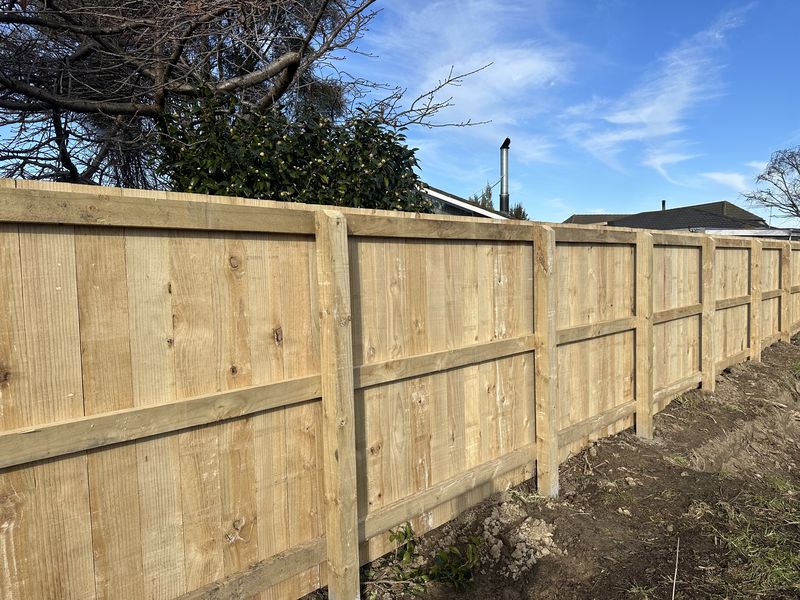 Timber paling fence with rails running the length of a boundary under a blue sky